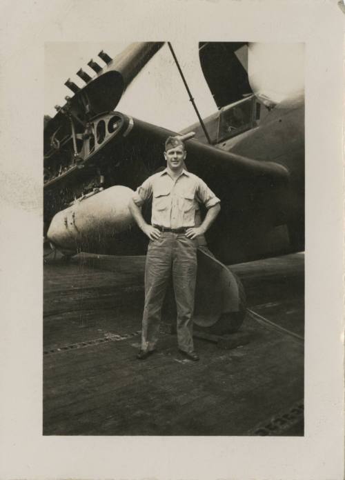 Black and white photograph of an officer standing next to a Curtiss SB2C Helldiver with folded …