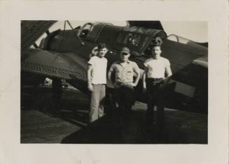 Black and white photograph of three men standing next to a Curtiss SB2C Helldiver with folded w…