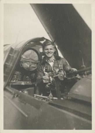 Black and white photograph of a man standing in an open gunner's compartment of a Curtiss SB2C …