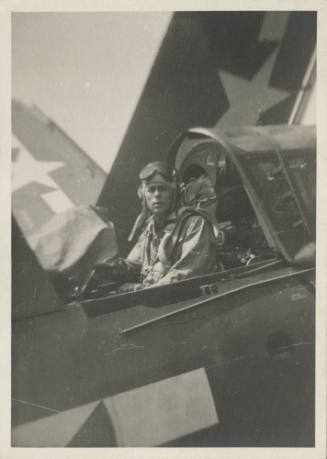 Black and white photograph of a man sitting in the rear gunner seat of a Curtiss SB2C Helldiver…