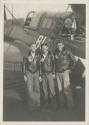 Black and white photograph of three men standing in front of the open cockpit of a Curtiss SB2C…