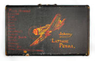 Black suitcase with yellow and red image of airplane banking to the right and name of owner in …