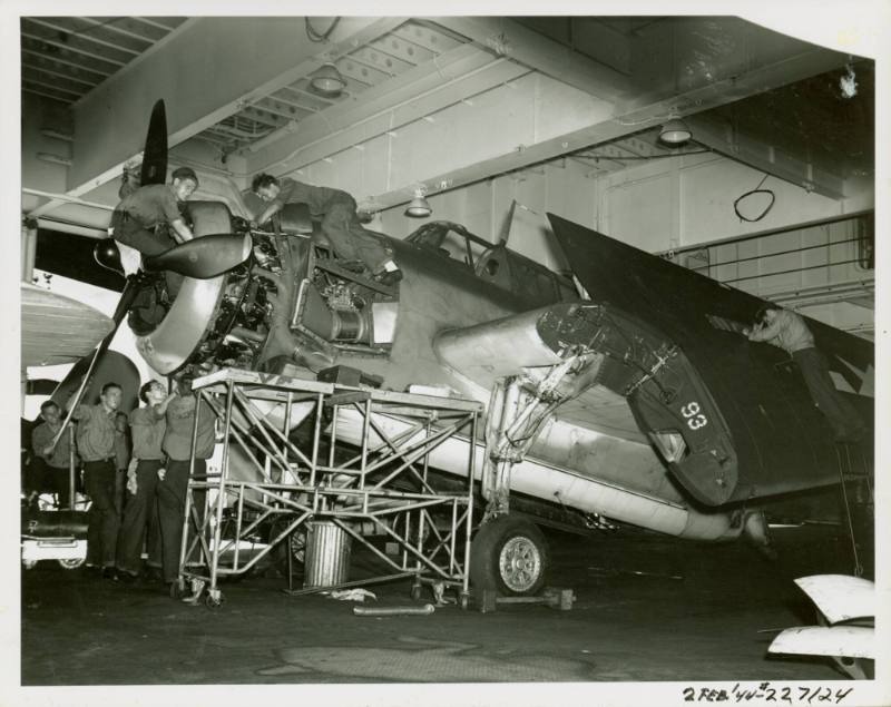 Mechanics in the hangar deck work on the engine and wing of a Grumman TBF-1C Avenger airplane