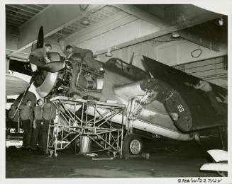 Mechanics in the hangar deck work on the engine and wing of a Grumman TBF-1C Avenger airplane
