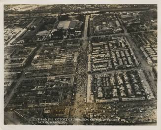 Black and white reconnaissance photograph of a large crowd of people in the streets of a densel…