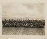 Black and white photograph of a large group of sailors posed in rows in the flight deck of the …