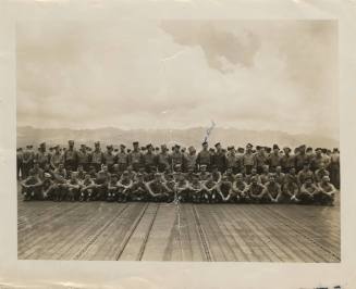 Black and white photograph of a large group of sailors posed in rows in the flight deck of the …
