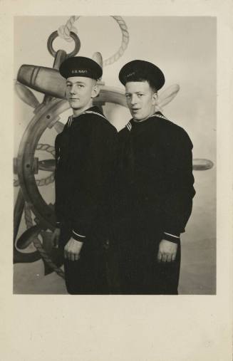 Black and white image of two men in US Navy dress blue uniforms standing in front of graphic of…