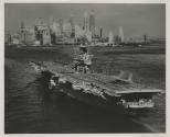 Black and white photograph of USS Intrepid sailing in New York harbor, lower Manhattan skyline …