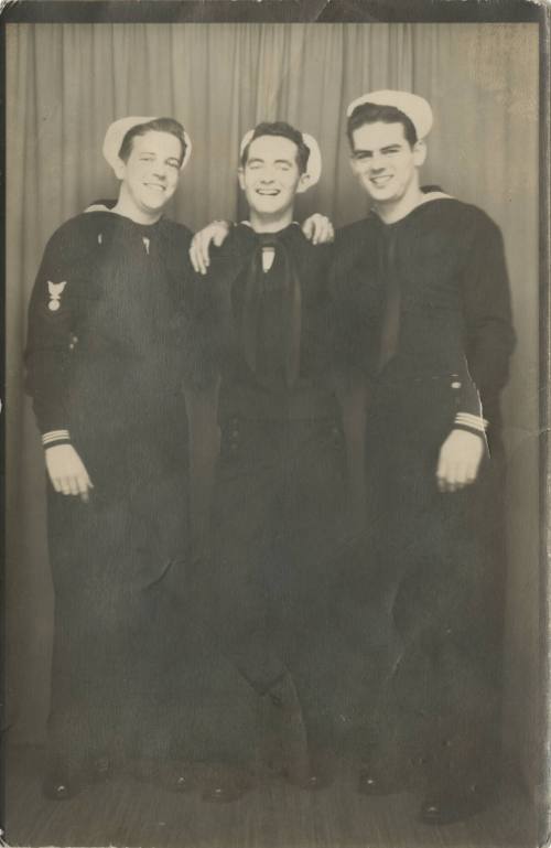 Black and white photograph of three smiling sailors in dress blue uniforms