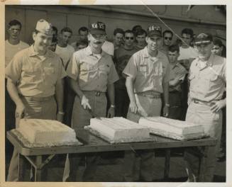 Black and white photograph of three officers standing behid three seperate cakes on USS Intrepi…