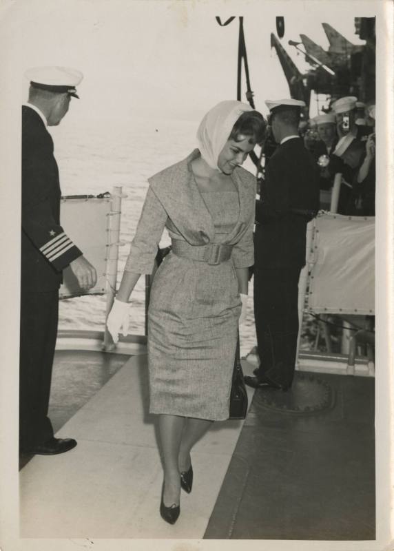 Black and white photograph of a woman with a scarf over her hair walking on board USS Intrepid