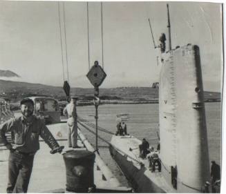 Black and white photograph of a man standing next to the submarine Growler anchored to a pier i…