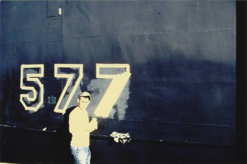 Color photograph of a sailor painting "577" in white on Growler's hull