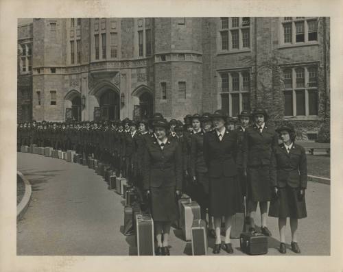 Black and white photograph of WAVES recruits in uniform with suitcases at their feet standing o…