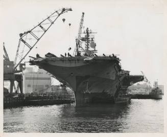 Black and white photograph of USS Intrepid in port with a crane over the ship