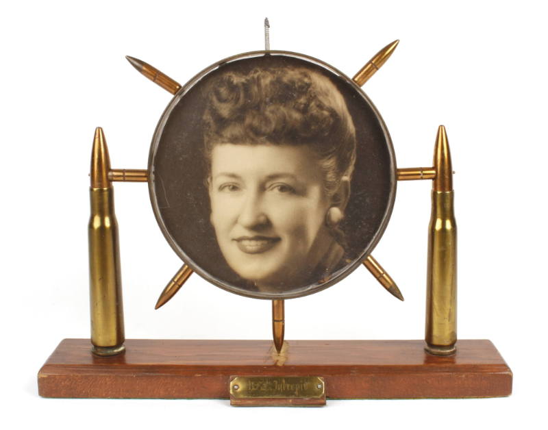 Circular picture frame ringed with seven bullets and supported by two larger bullets on either …