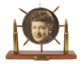 Circular picture frame ringed with seven bullets and supported by two larger bullets on either …