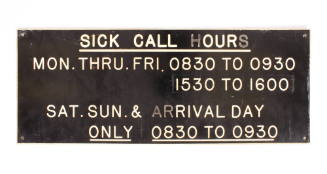 Rectangular black sign with sick call days and hours in white lettering