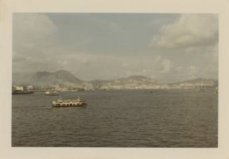 Color photograph of Victoria Harbor with ships visible on water and city on the shore in the di…