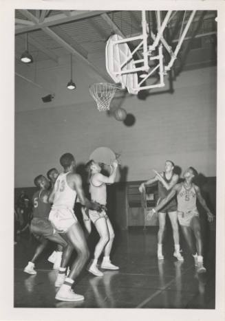 Black and white photograph of USS Intrepid’s basketball team in white jerseys playing against a…