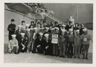 Black and white photograph of a group of children and sailors standing next to USS Intrepid wit…