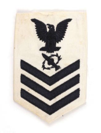 White U.S. Navy uniform patch with dark blue eagle, chevrons and image of a missile with a jagg…
