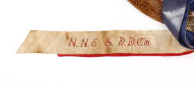 White ribbon with "N.N.S & D.D.Co." red embroidered text