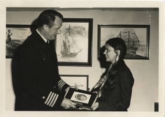 Black and white photograph of USS Intrepid's commanding officer handing a plaque to Miss Intrep…