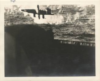 Printed black and white photograph of a Japanese kamikaze aircraft being shot down just off the…