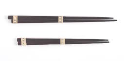 Two pairs of dark brown or black souvenir chopsticks, a longer pair above and a shorter pair be…