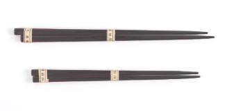 Two pairs of dark brown or black souvenir chopsticks, a longer pair above and a shorter pair be…