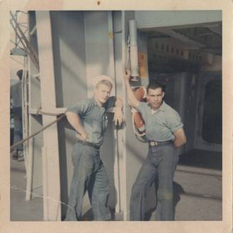 Color photograph of two men leaning on the outer ship's bulkhead