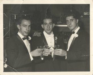 Black and white photograph of three men in tuxedos raising their drinking glasses 