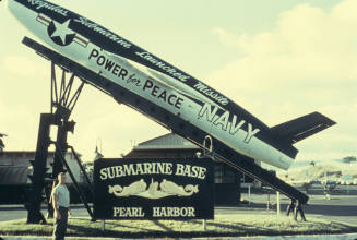 Color photograph of entrance to submarine base at Pearl Harbor, a man stands below Regulus I mi…