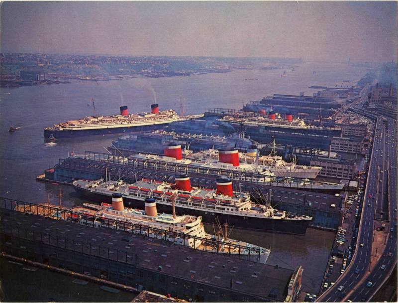 Color postcard with a photograph of piers on the Hudson River with 6 ships, including USS Intre…