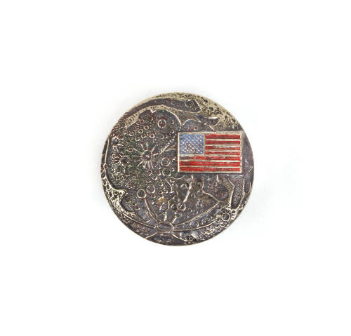 Circular commemoration pin depicting the surface of the moon with a colored American flag in th…