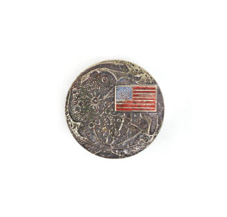 Circular commemoration pin depicting the surface of the moon with a colored American flag in th…