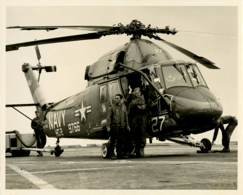 Black and white photograph of two men exiting a helicopter on the flight deck of USS Intrepid