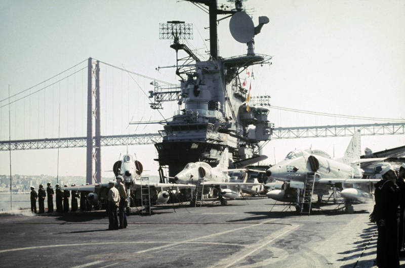 Color photograph of USS Intrepid sailing into or out of port, with crew members manning the rai…