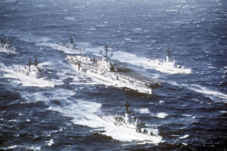 Color photograph of Intrepid at sea among a fleet of other ships