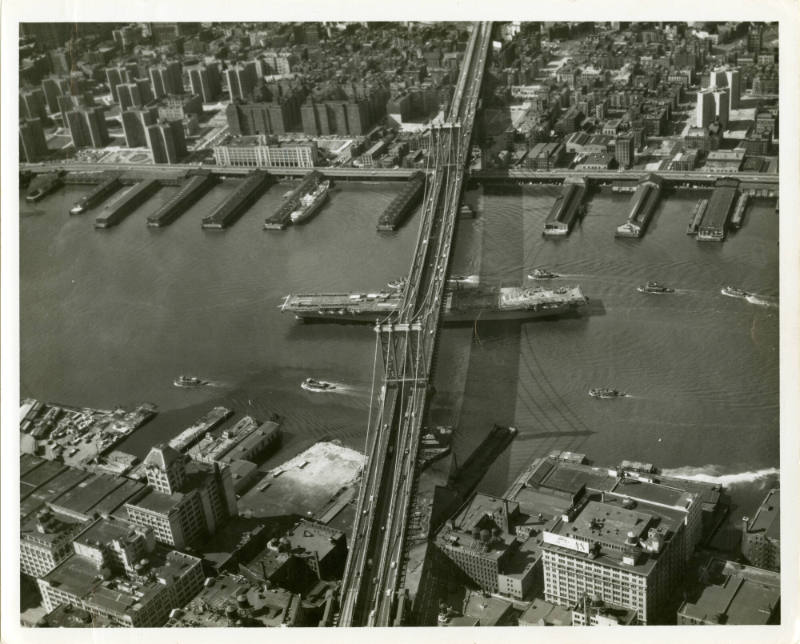 Black and white photograph of USS Intrepid sailing under the Manhattan Bridge in New York CIty