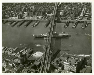Black and white photograph of USS Intrepid sailing under the Manhattan Bridge in New York CIty