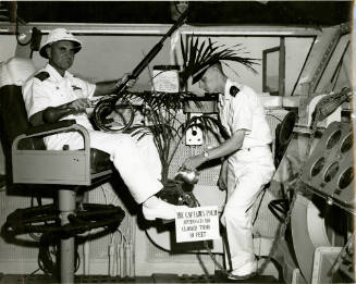 Black and white photograph of Captain Abbott sitting in the captain's chair with a potted palm …