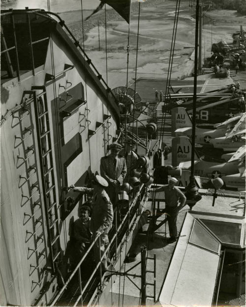 Black and white photograph of an officer painting USS Intrepid's Battle Efficiency "E" on the s…