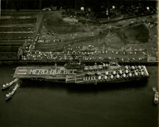 Black and white aerial photograph of USS Intrepid in port with sailors in formation spelling "M…