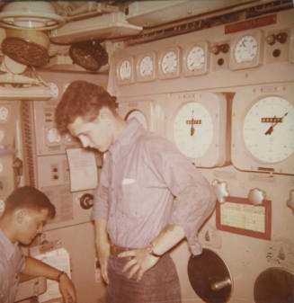 Printed color photograph of two sailors in the maneuvering room on the submarine USS Growler