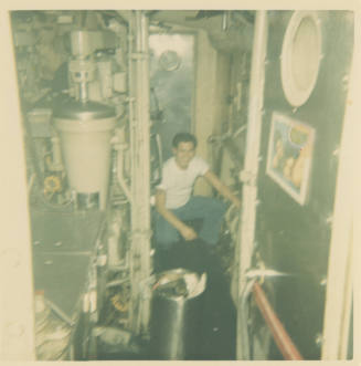 Printed color photograph of a sailor crouching in the submarine USS Growler's engine room