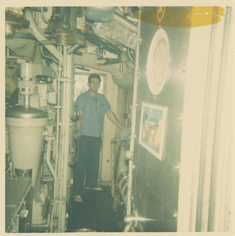 Printed color photograph of a sailor standing in the submarine USS Growler's engine room