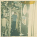 Printed color photograph of a sailor standing in the submarine USS Growler's engine room